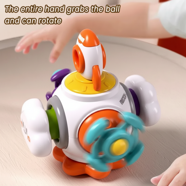 Hands beside a Rocket activity toy with a teal steering wheel and orange rocket on a tabletop