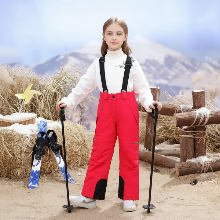 Child wearing rosé red ski pants with black suspenders and holding ski poles.