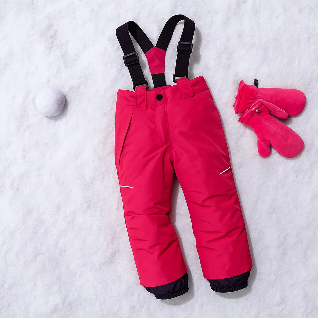 Rosé red ski pants laid on snow with black suspenders, dark lower-leg panels and pink mittens nearby.