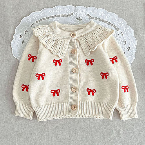 Red bow details on a white knit cardigan with a ruffled neckline and button front