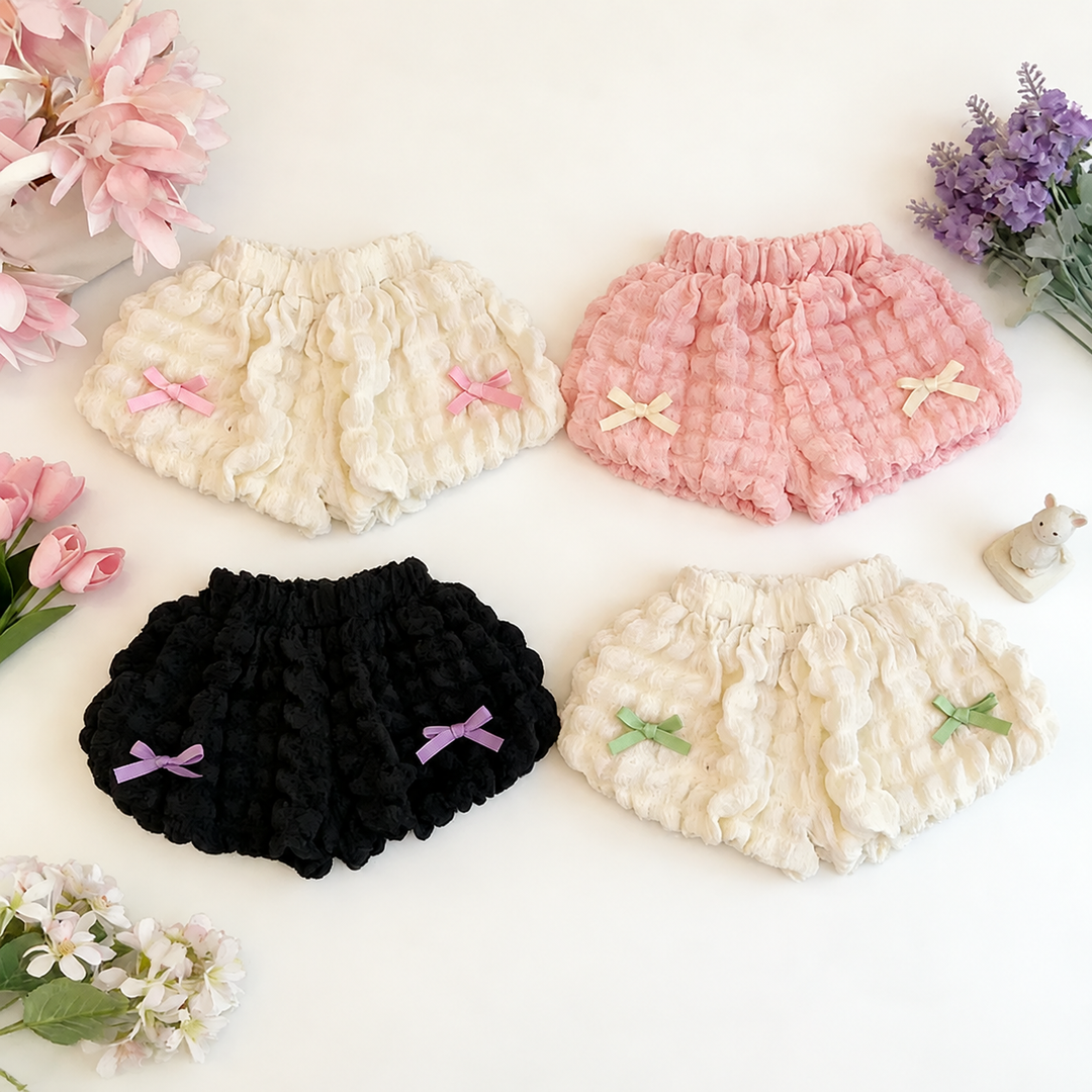 Four pairs of kids' ruffle shorts in cream, pink, and black with contrasting bows