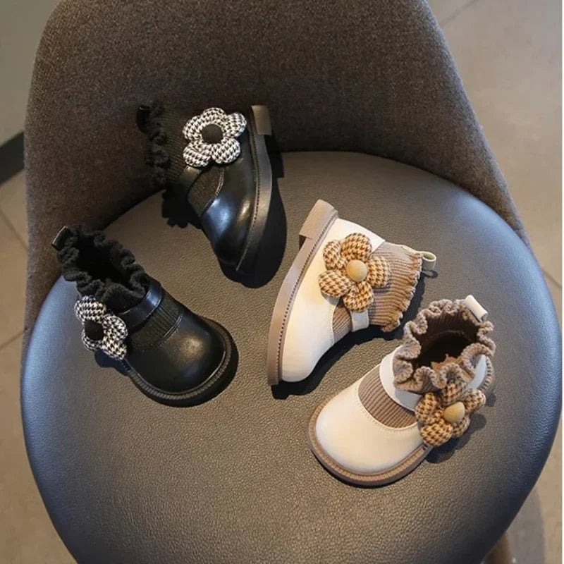White and black girls' boots arranged on a chair, showing flower accents and ruffled cuffs