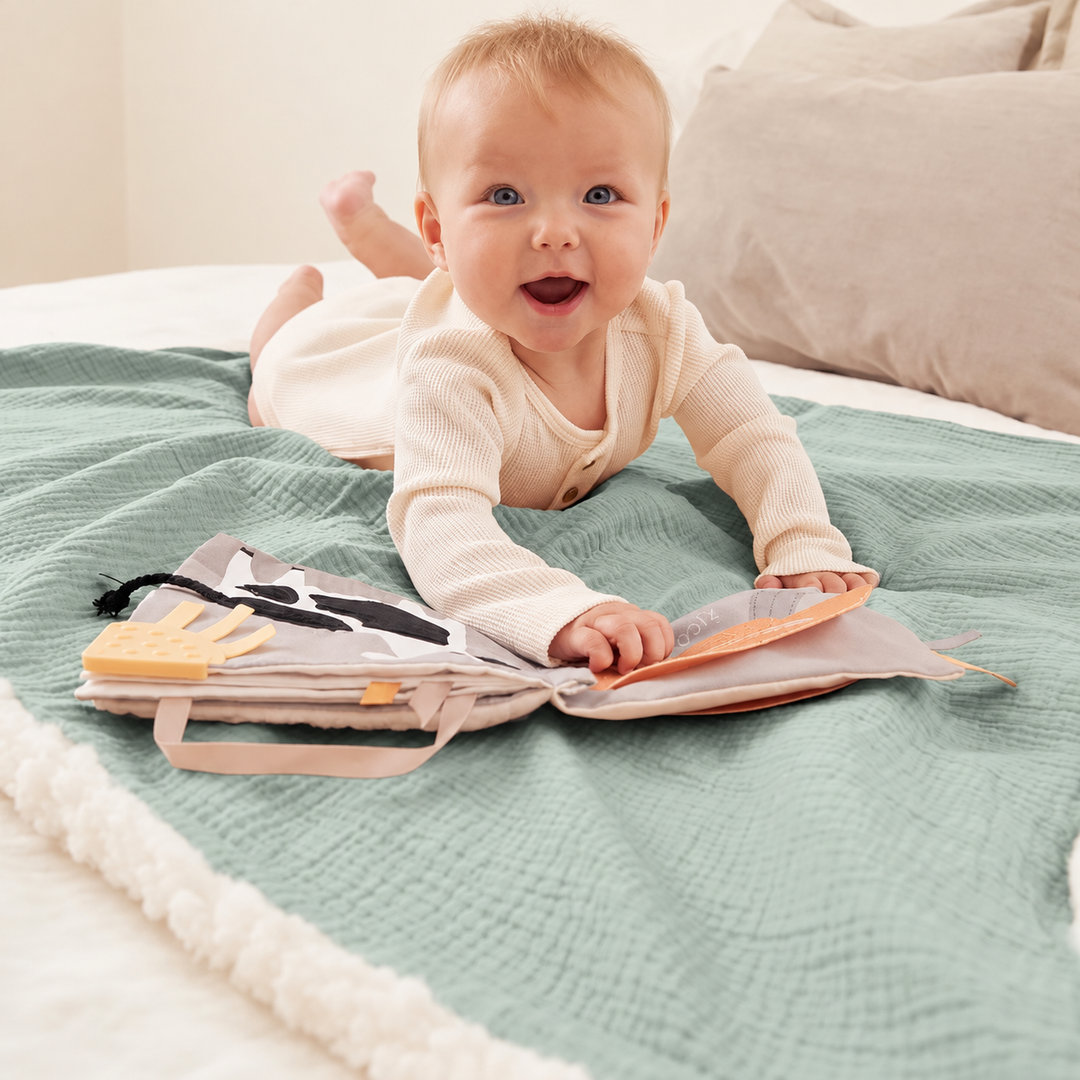 Baby exploring a cloth book on a sage green blanket with white sherpa edging