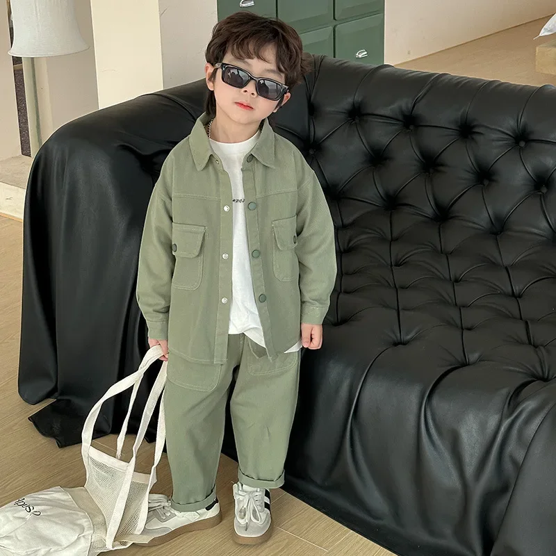 Child in the sage green button-front shirt and matching cargo pants beside a black sofa