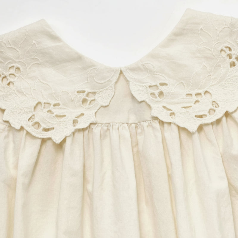 Close-up of the cream dress collar with scalloped edges and floral eyelet detailing