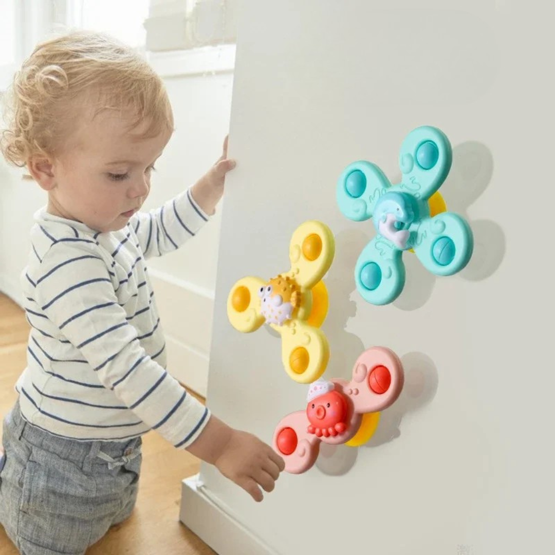 Toddler reaching for three ocean-animal suction spinners attached to a white vertical surface