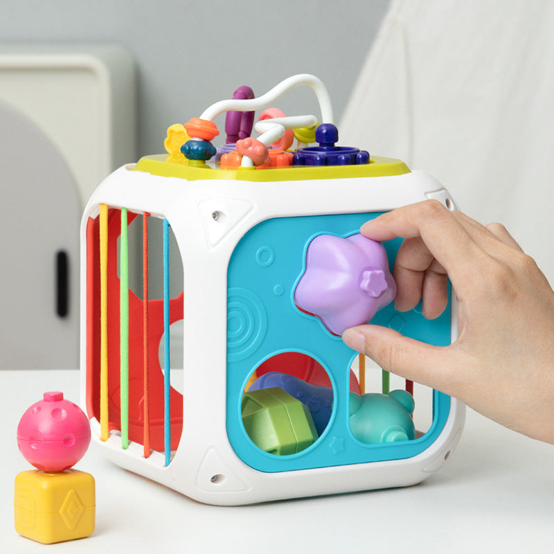 Hand fitting a purple heart-shaped piece into the turquoise side of a colorful shape sorter cube