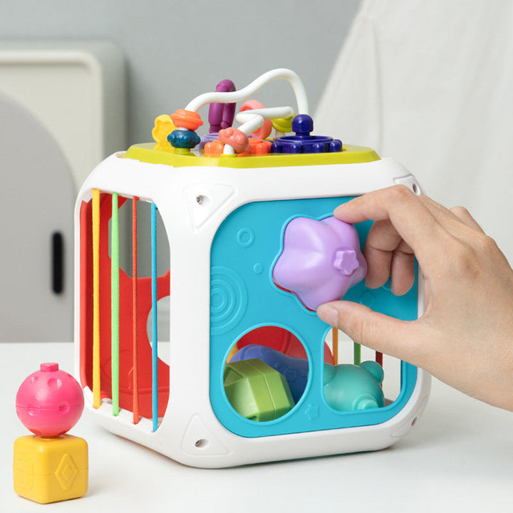 Hand fitting a purple heart-shaped piece into the turquoise side of a colorful shape sorter cube