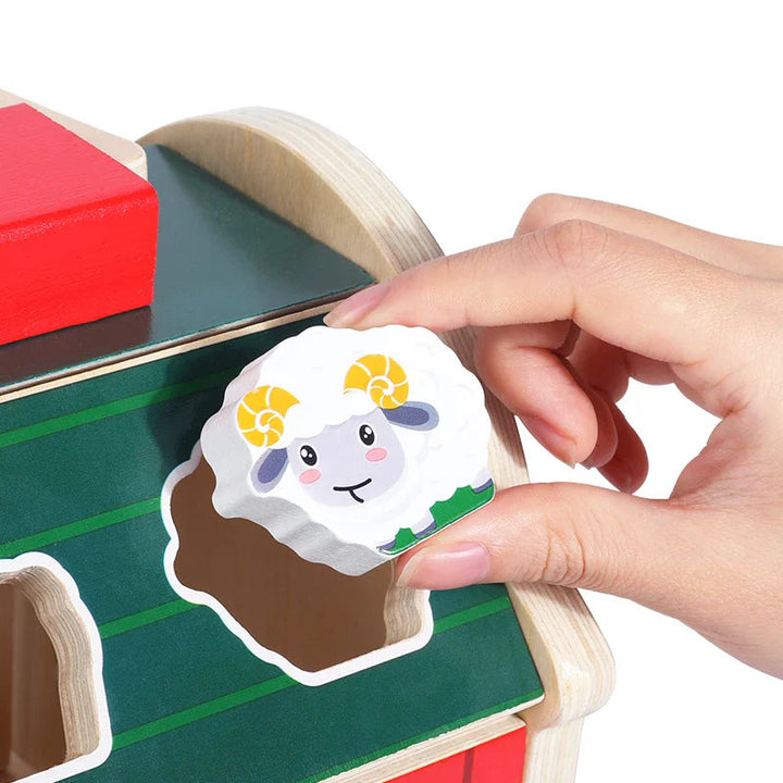 A hand matching a wooden sheep piece to a shaped opening in the barn roof.