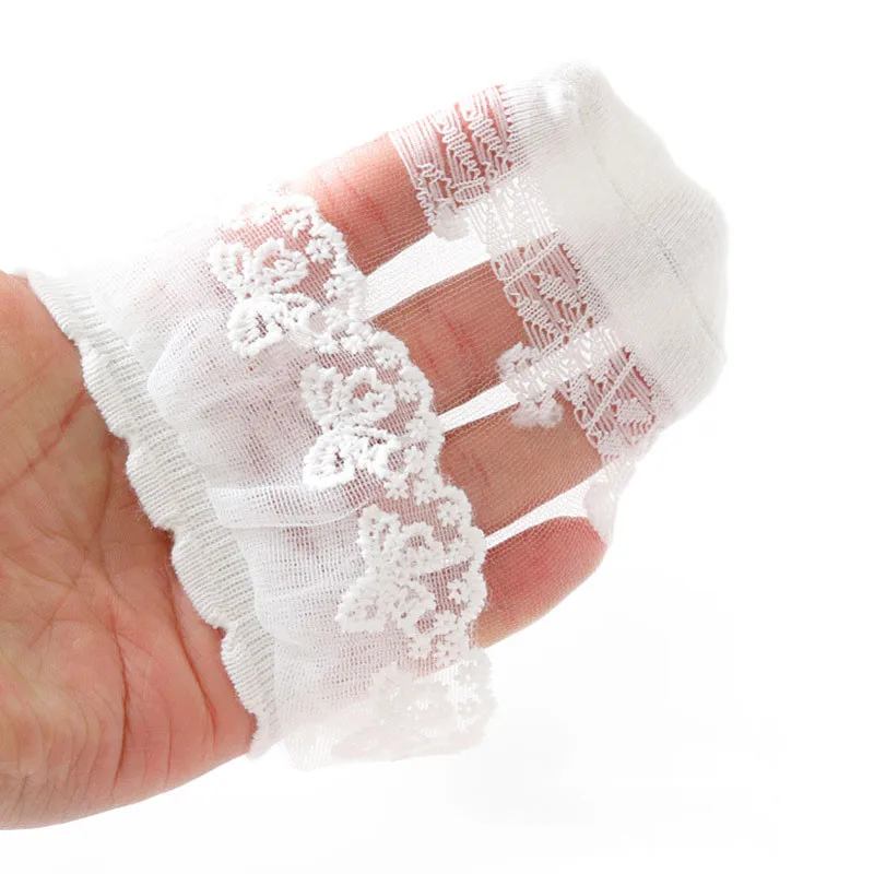 White lace baby sock held across a hand to show the sheer mesh and floral embroidery.