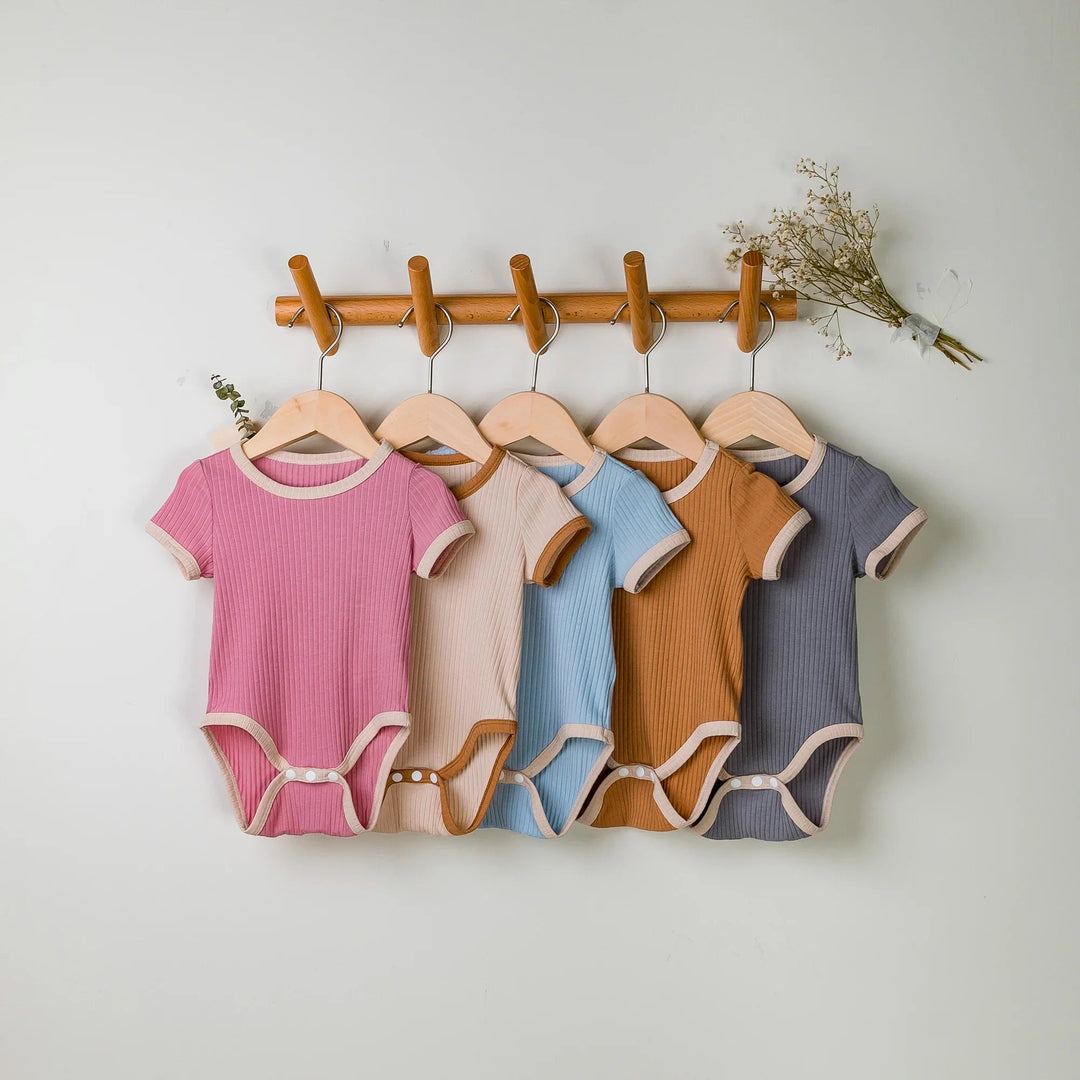 Five short-sleeve baby rompers with contrast trim on wooden hangers