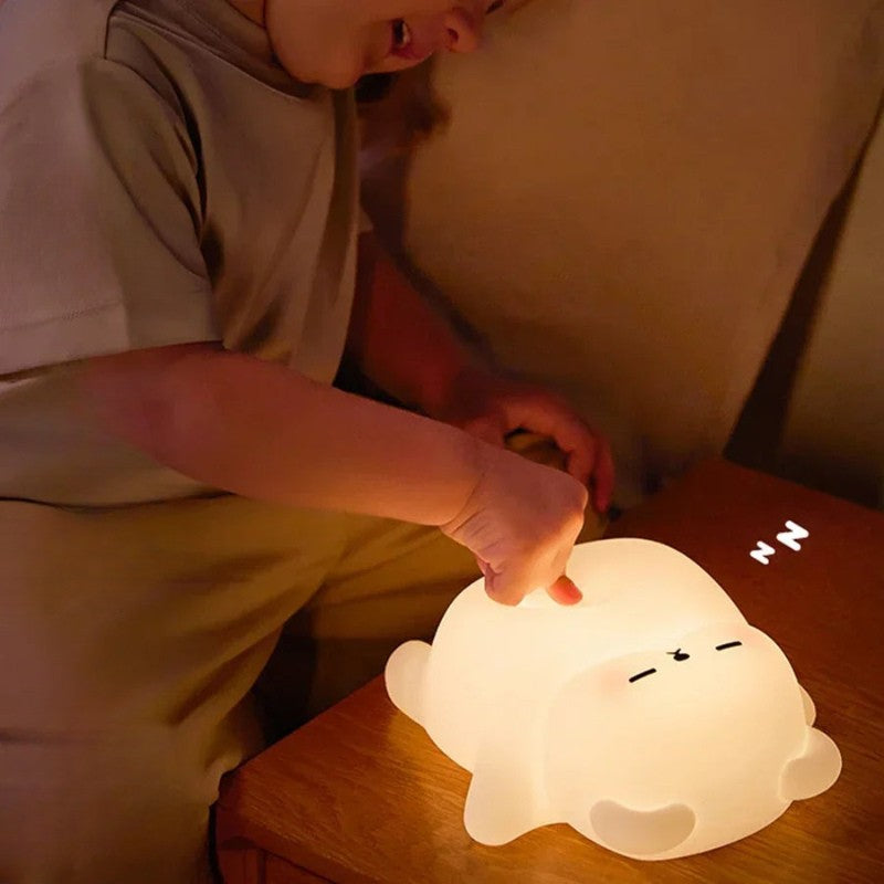 Child pressing the top of a glowing bear-shaped night light on a bedside table