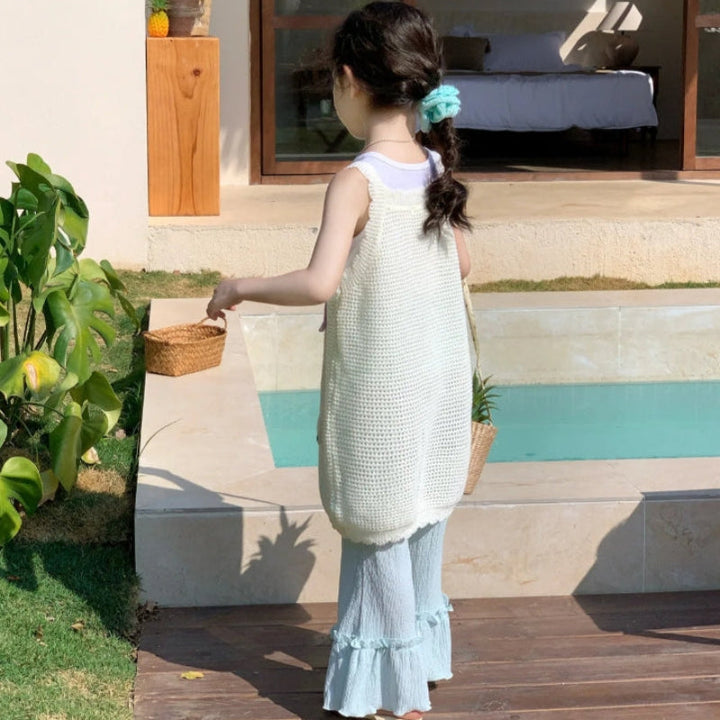 Back view of the cream sleeveless top and pale green ruffled pants beside a pool