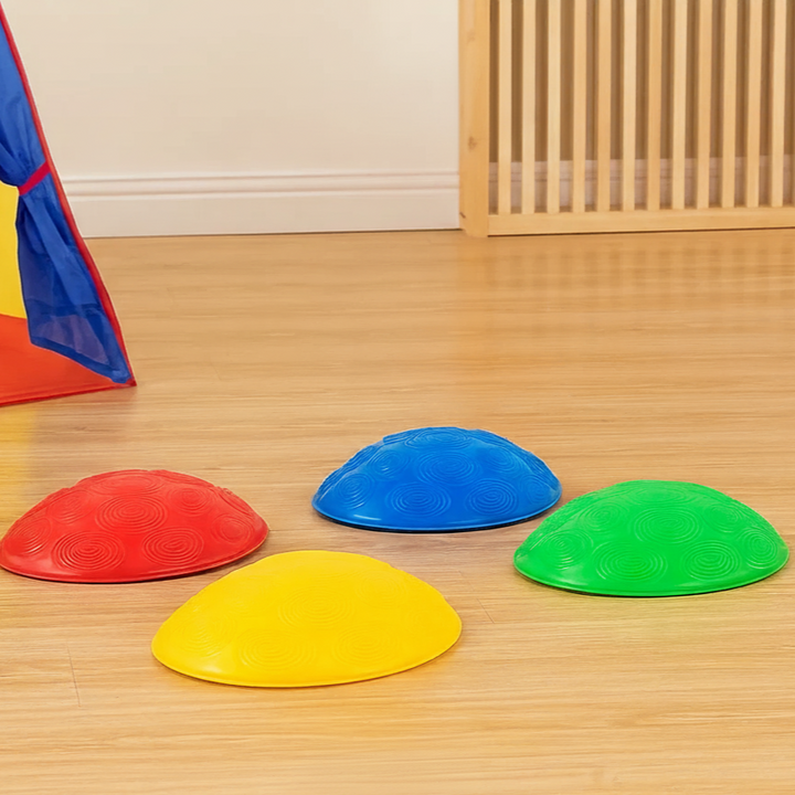 Four small shell-shaped stepping stones in red, blue, green, and yellow on a wooden floor