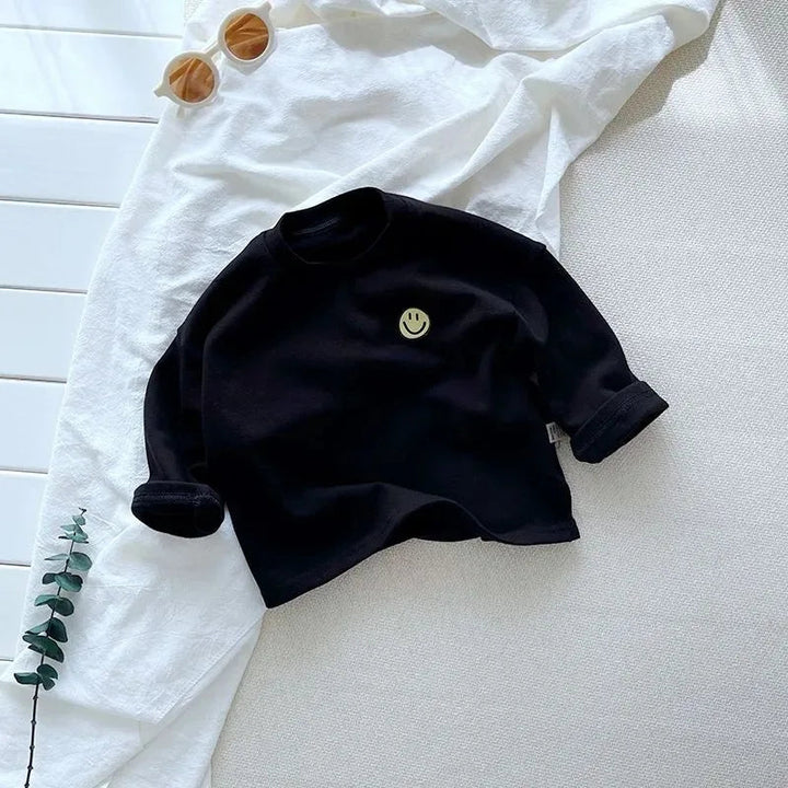 Solid black crew-neck shirt with long sleeves and a small smile patch on the chest.