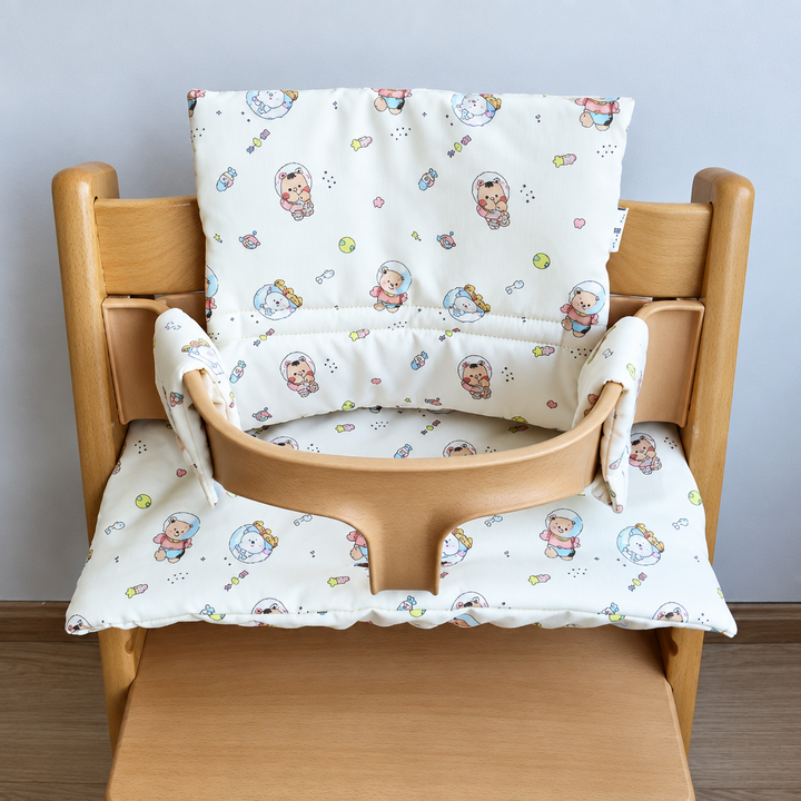 White high chair cushion with a colorful space-bear print on a wooden chair