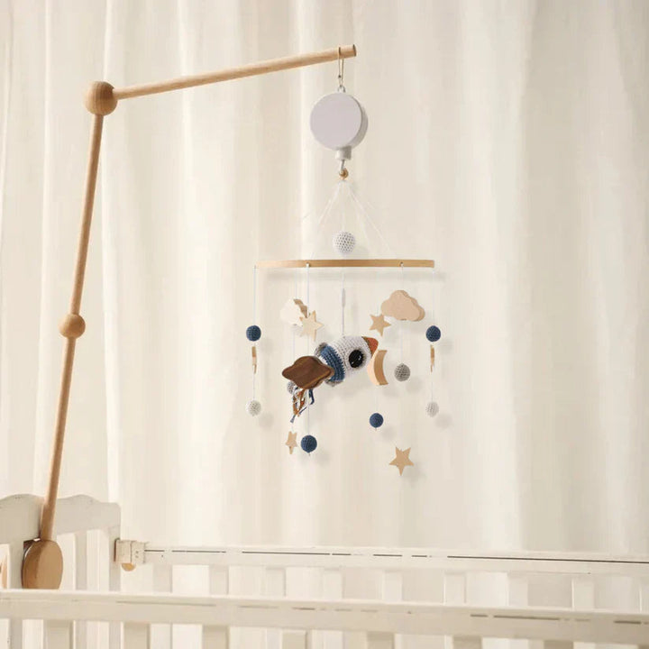 Space rocket baby mobile hanging from a wooden mounting arm above a white crib