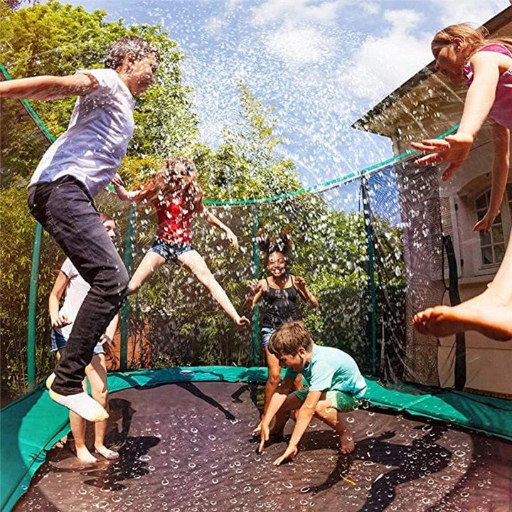 Children jumping through water spray on a backyard trampoline.