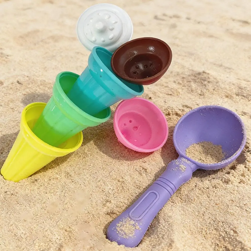 Colorful cone-shaped cups stacked beside ice cream molds and a purple sand scoop on the beach
