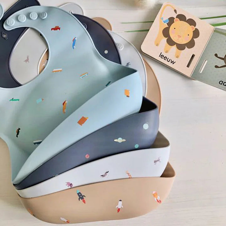 Stacked silicone baby bibs with printed designs and curved food-catching pockets