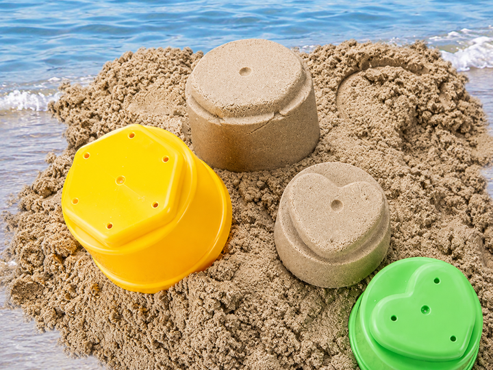 Yellow and green stacking cups beside cup-shaped sand towers at the beach