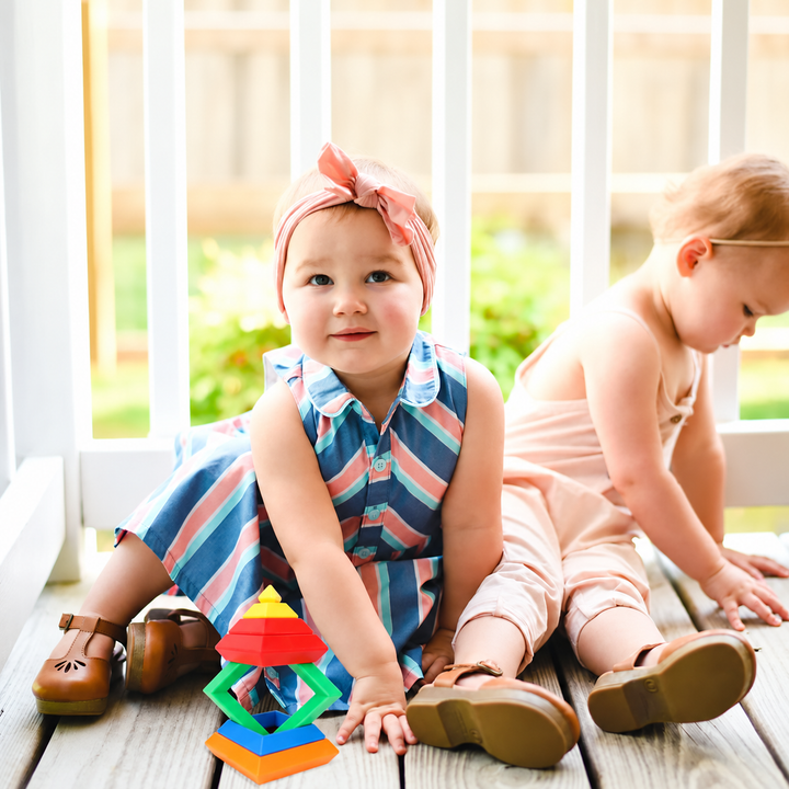 Two children seated by a window with a colorful stacking block tower