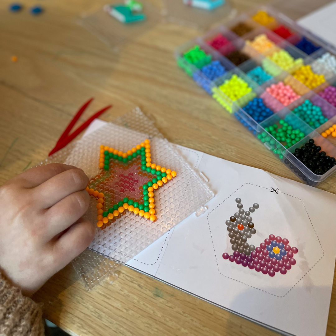 Star-shaped bead design on a clear plate beside pattern cards and a multicolored bead tray