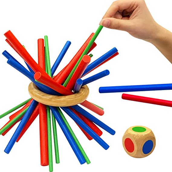 A hand lifts a green stick from a colorful wooden balance game beside a color-marked die.