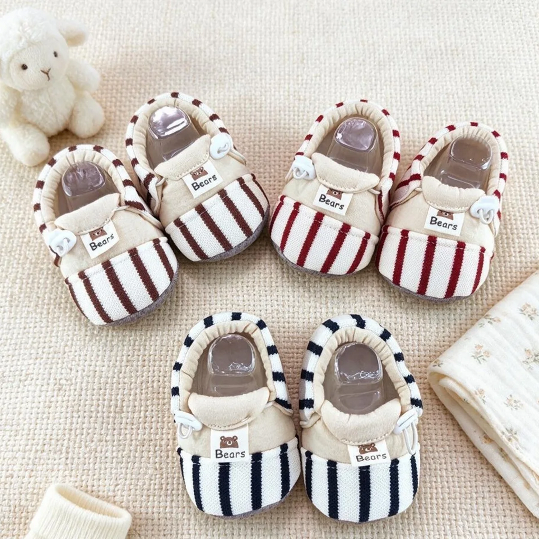 Striped baby shoes in brown, red, and black arranged on a cream blanket