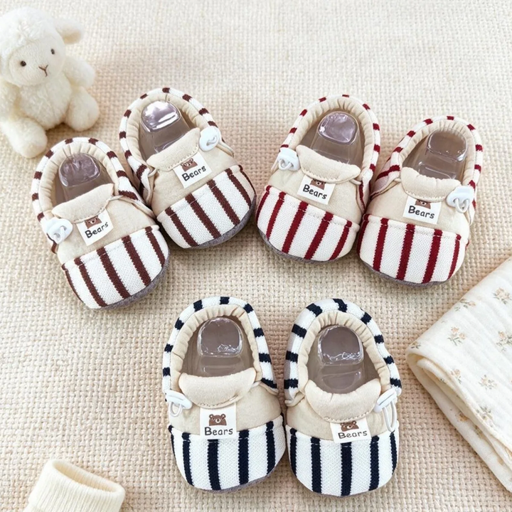 Striped baby shoes in brown, red, and black arranged on a cream blanket