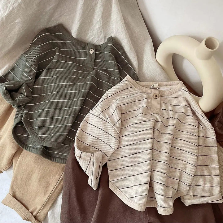 Two striped cotton shirts with button necklines displayed with neutral-colored pants