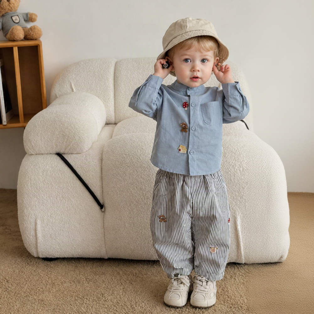 Child wearing striped embroidered pants with a light blue shirt, beige hat, and sneakers.