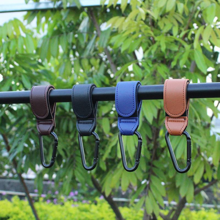 Four stroller hooks in different colors hanging from an outdoor rail