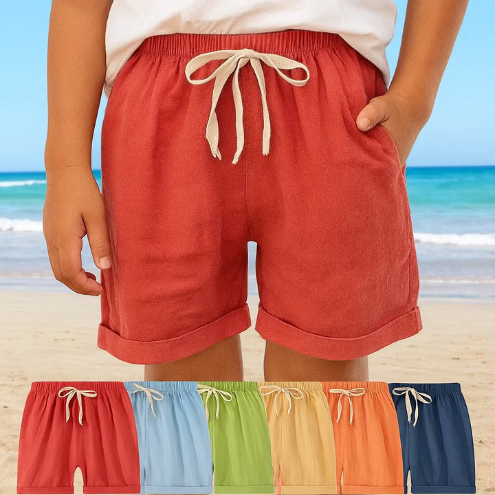Child wearing red drawstring shorts at the beach, with six color options pictured below