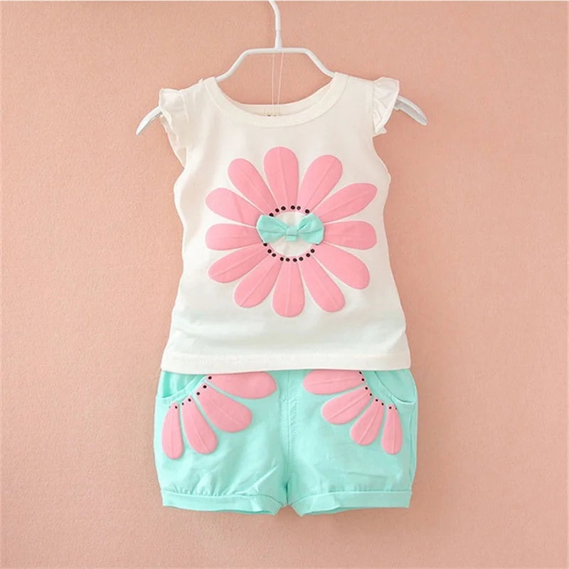 White baby top with a pink flower and aqua bow, paired with aqua floral shorts