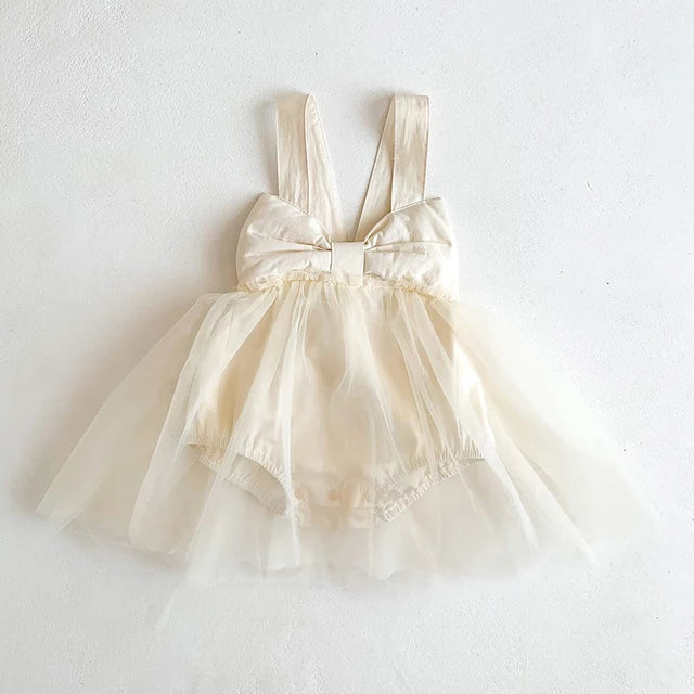 Apricot baby romper dress with wide shoulder straps, a large bow and a sheer skirt overlay.