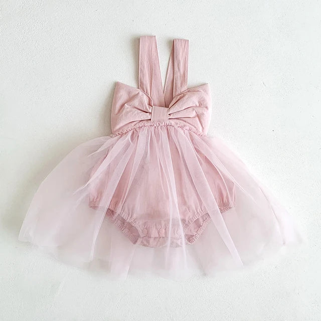 Pink baby romper dress with a large bow, wide shoulder straps and a floaty sheer skirt.