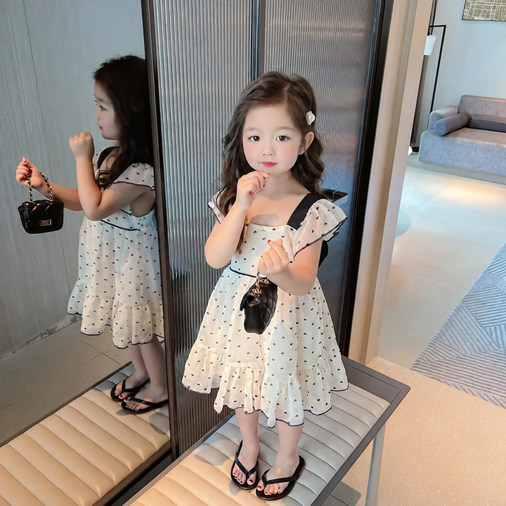 Girl wearing a cream heart-print dress with ruffled shoulders and black waist trim