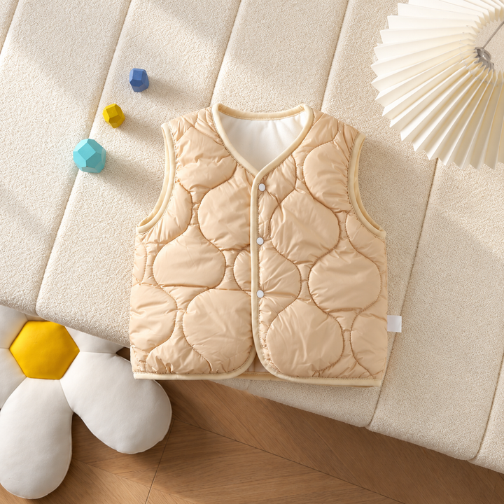 Tan quilted baby vest with front snaps laid on a cream cushion.
