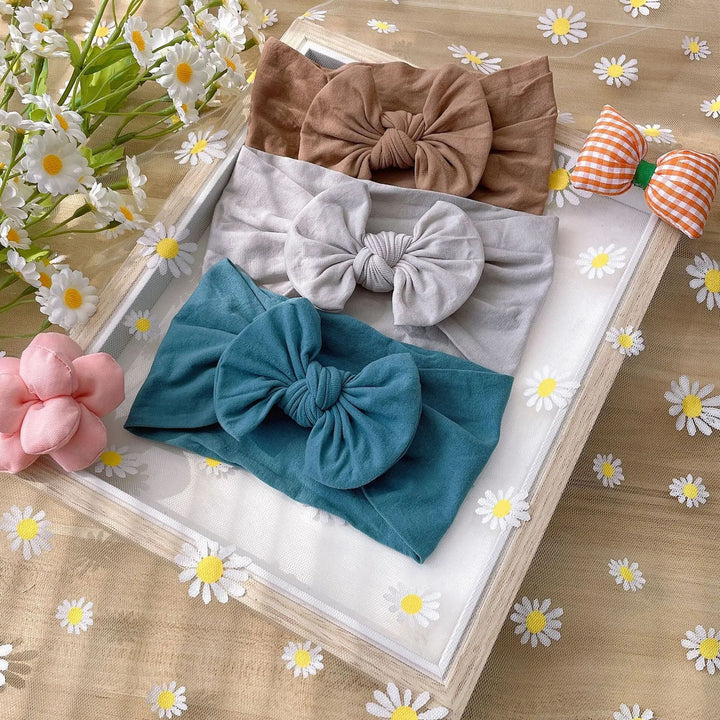 Teal, gray, and brown bow headbands displayed together beside daisies
