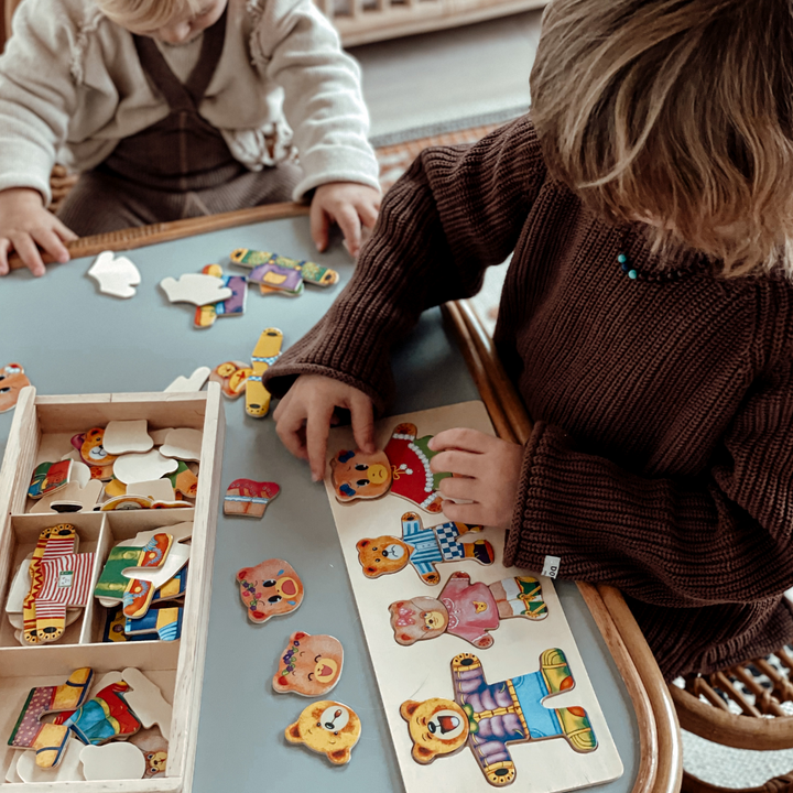 Two children mixing wooden bear dress-up puzzle pieces at a table