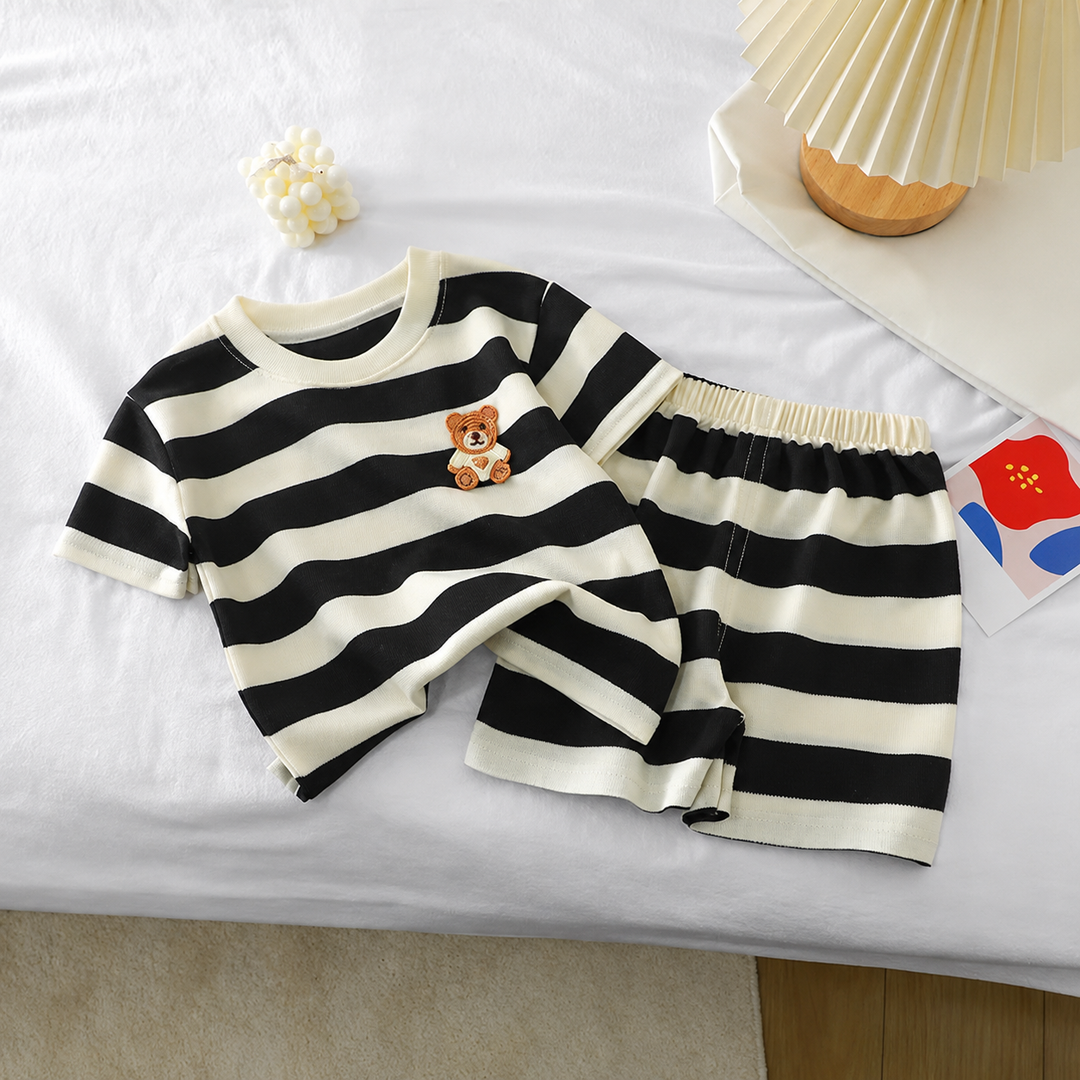 Teddy bear T-shirt and matching striped shorts laid out together on bedding
