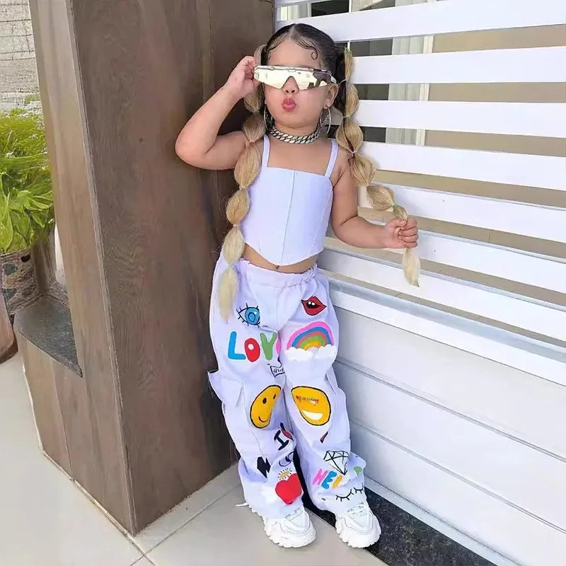 Child modeling a thin-strap crop top and white pants covered in colorful lettering and playful graphics