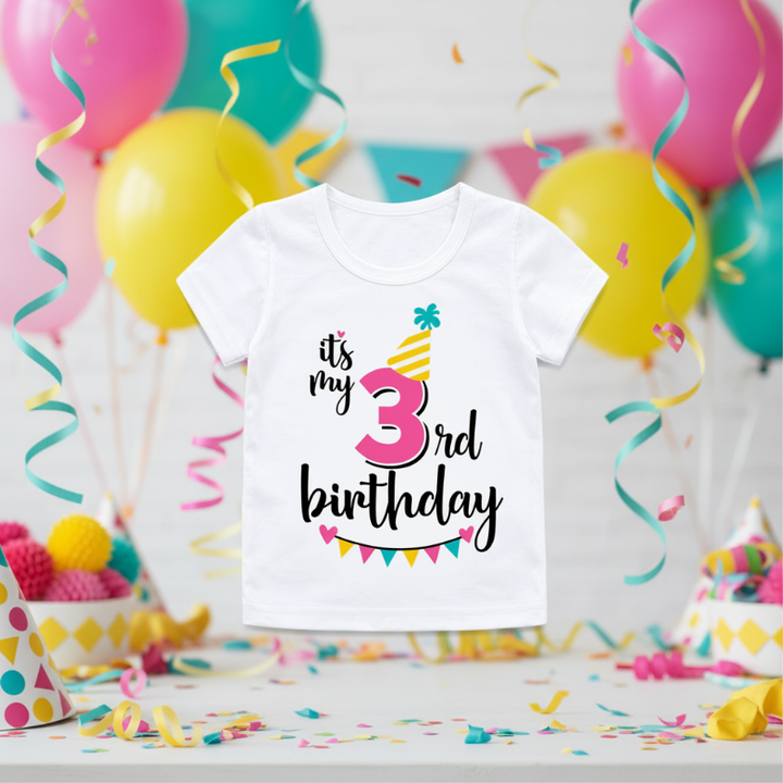 White third-birthday T-shirt with a pink number 3, yellow party hat, and colorful bunting