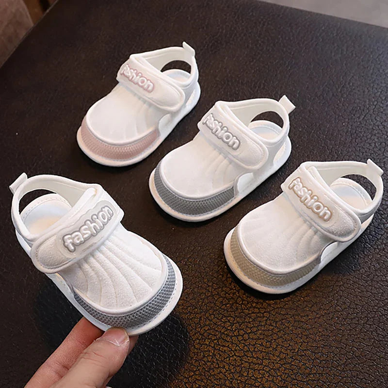 Three baby sandals with pink, gray, and beige trim on a dark surface