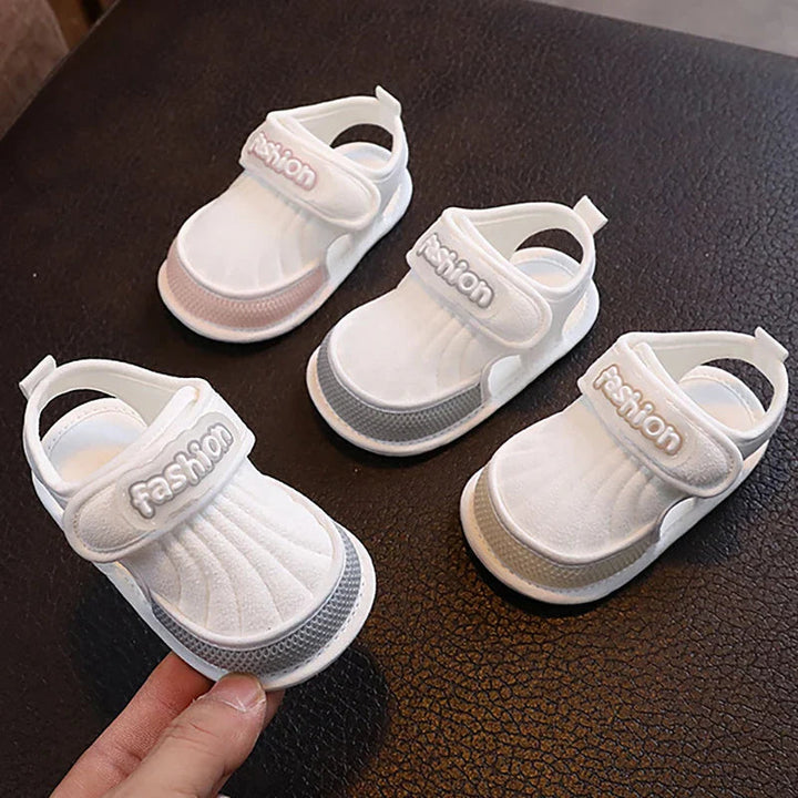 Three baby sandals with pink, gray, and beige trim on a dark surface