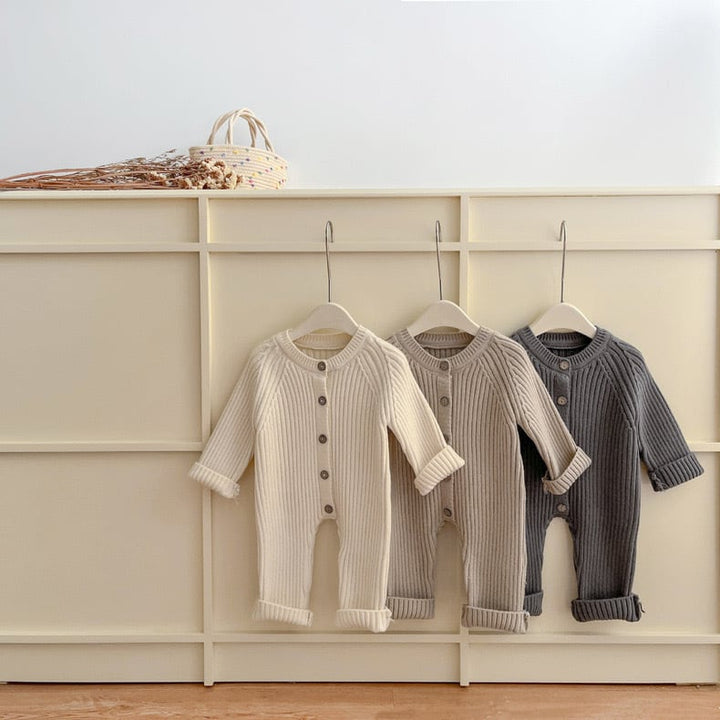 Cream, khaki, and gray baby rompers hanging from a wall rack