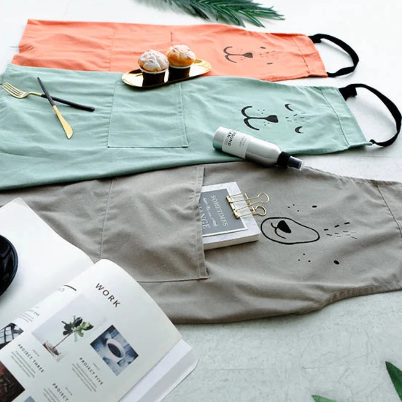 Red, green, and gray bear aprons laid flat with kitchen utensils and baked treats