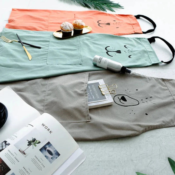 Red, green, and gray bear aprons laid flat with kitchen utensils and baked treats
