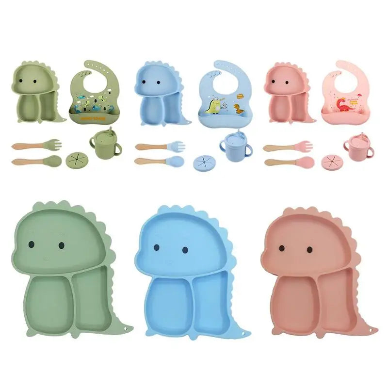 Green, blue, and pink dinosaur tableware sets with matching divided plates, bibs, cups, and utensils